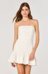 A woman is wearing a strapless white dress with horizontal ruching along the bodice and a ruffled, gathered hem.